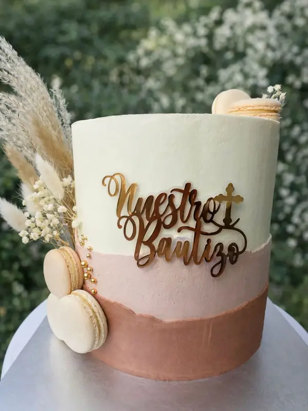 Torta de bautizo en tonos crema y rosa viejo con topper dorado «Nuestro Bautizo» y macarons